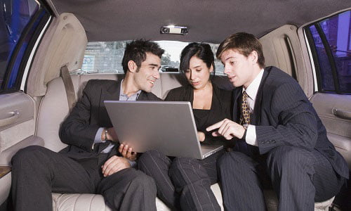 Business executives in the back of a limo sitting together reviewing a presentation on one of their laptops in preparation for a business conference.